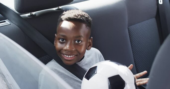 African American boy smiles in the backseat of a car, holding a soccer ball