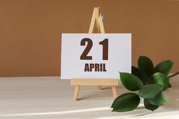 April 21th. Day 21 of month, Calendar date. Green branch, easel with the date and month on desktop....