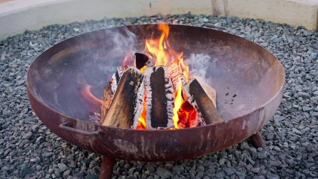 Portable camping metal fire pit on stone ground with burning fire outdoors.
