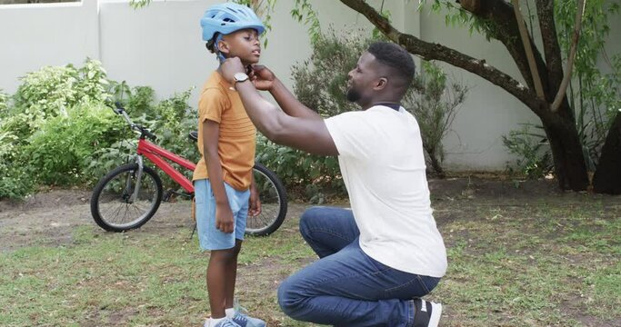 African American father helps a son with his helmet outdoors