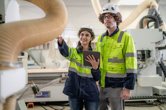 Industrial engineer wear helmet and safety uniform working in heavy engineering factory. Confident technician woman and colleague worker operating automated machine in manufacturing facility workshop