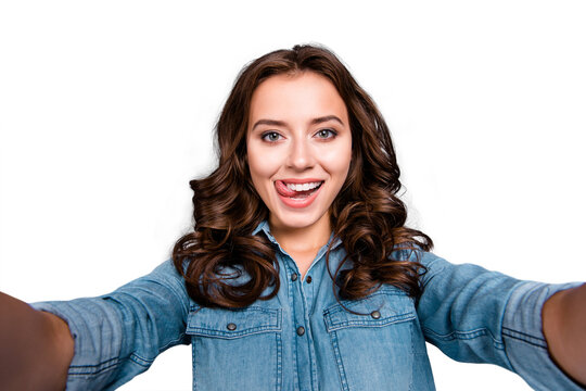 Self-portrait of nice cute stylish trendy flirty cheerful lovely attractive adorable brunette girl with wavy hair in casual denim shirt, showing tongue out, isolated over grey background