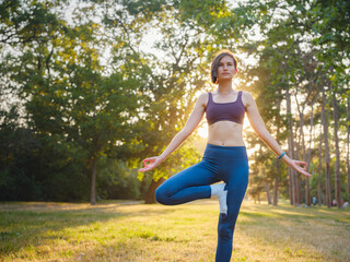Young asian woman doing yoga in morning or evening at park, healthy woman relaxing and practicing tree pose at city park. Mindfulness, destress, Healthy habits and balance concept