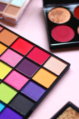 Various colorful eyeshadow palettes on bright pink background. Selective focus.