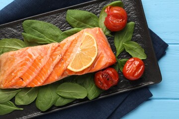 Tasty grilled salmon with tomatoes, spinach and lemon on light blue table, top view