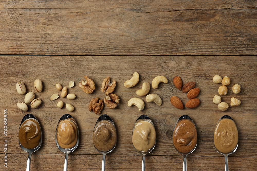 Sticker Tasty nut butters in spoons and raw nuts on wooden table, flat lay. Space for text