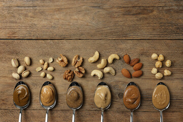Tasty nut butters in spoons and raw nuts on wooden table, flat lay. Space for text
