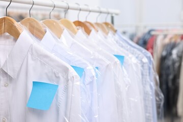 Dry-cleaning service. Many different clothes in plastic bags hanging on rack indoors, closeup