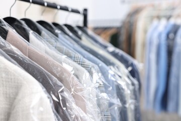 Dry-cleaning service. Many different clothes in plastic bags hanging on rack indoors, closeup