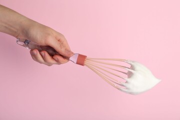 Naklejka premium Woman holding whisk with whipped cream on pink background, closeup