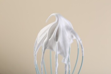 Whisk with whipped cream on beige background, closeup