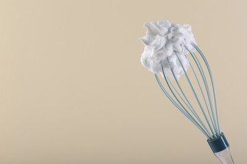 Whisk with whipped cream on beige background. Space for text