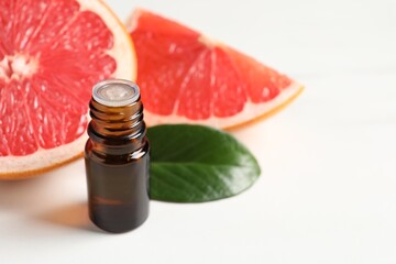 Grapefruit essential oil in bottle, leaf and fruit on white table, closeup. Space for text