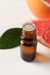 Grapefruit essential oil in bottle, leaf and fruit on white table, closeup