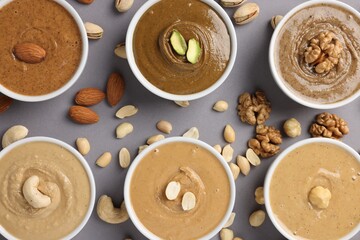 Many tasty nut butters in bowls and nuts on grey table, flat lay