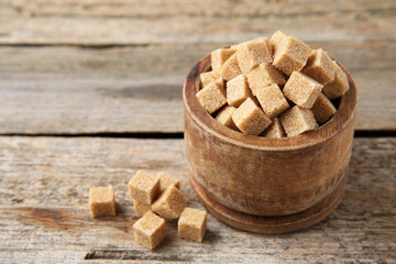 Bowl with brown sugar cubes on wooden table, closeup. Space for text