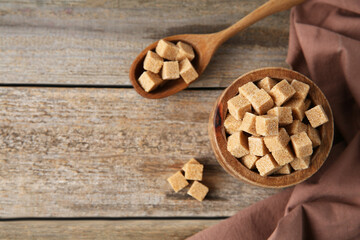 Bowl and spoon with brown sugar cubes on wooden table, flat lay. Space for text