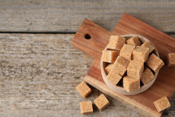 Bowl with brown sugar cubes on wooden table, above view. Space for text
