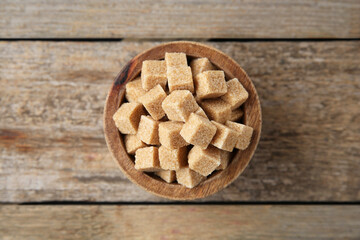 Bowl with brown sugar cubes on wooden table, top view