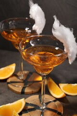 Tasty cocktails in glasses decorated with cotton candy and orange slices on gray table, closeup