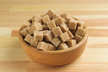 Brown sugar cubes in bowl on wooden table, closeup