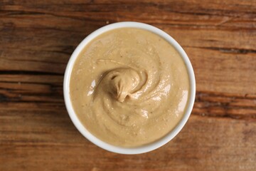 Delicious nut butter in bowl on wooden table, top view
