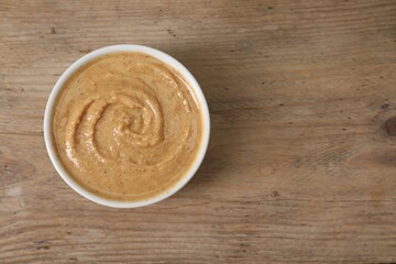 Delicious nut butter in bowl on wooden table, top view. Space for text