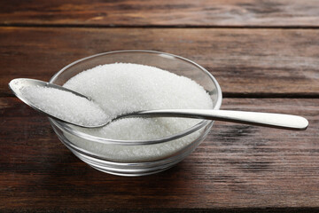 Granulated sugar in bowl and spoon on wooden table, closeup