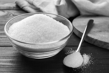 Granulated sugar in bowl and spoon on black wooden table, closeup