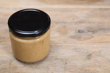 Tasty nut paste in jar on wooden table, closeup. Space for text