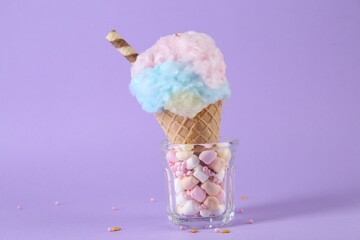 Sweet cotton candy in waffle cone on purple background, closeup