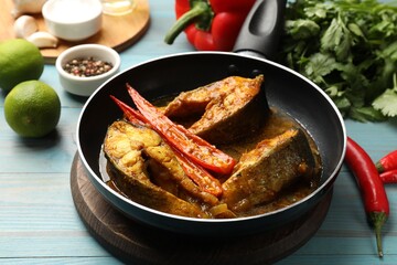 Tasty fish curry in frying pan and ingredients on light blue wooden table, closeup. Indian cuisine