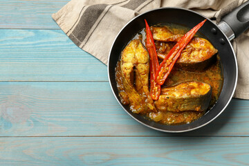Tasty fish curry in frying pan on light blue wooden table, top view. Space for text. Indian cuisine