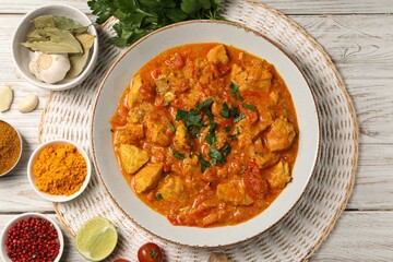 Delicious chicken curry and ingredients on wooden table, flat lay