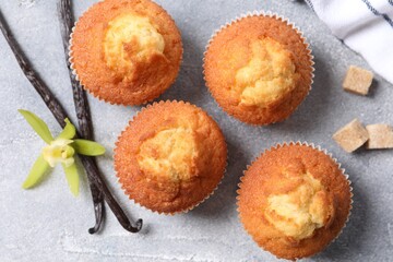Delicious sweet muffins, vanilla pods and brown sugar on light grey textured table, flat lay