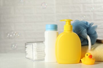 Baby cosmetic products, bath duck, cotton swabs and towel on white table against soap bubbles. Space for text