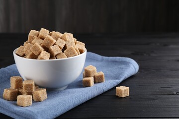 Brown sugar cubes on black wooden table, space for text