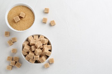 Fototapeta na wymiar Brown granulated sugar and cubes on white textured table, flat lay. Space for text