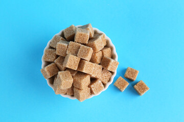 Brown sugar cubes in bowl on light blue background, top view