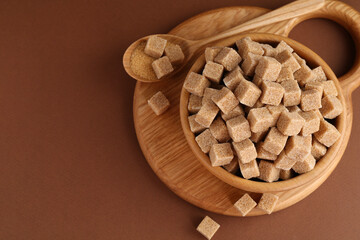 Brown sugar cubes in bowl and spoon on color background, top view. Space for text