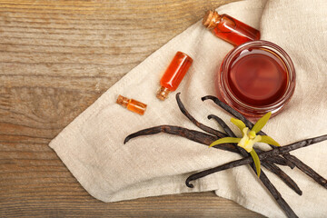 Aromatic vanilla extract, pods and flower on wooden table, top view