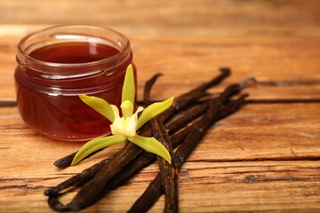 Aromatic vanilla extract, pods and flower on wooden table, closeup. Space for text