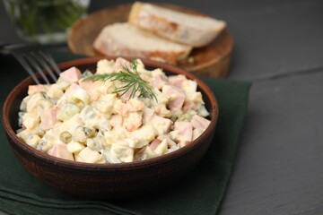Tasty Olivier salad with boiled sausage in bowl on grey table, closeup. Space for text