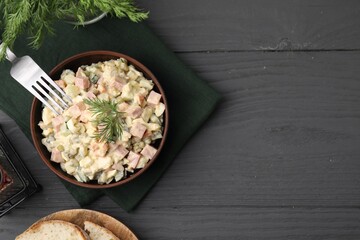 Tasty Olivier salad with boiled sausage in bowl served on grey wooden table, flat lay. Space for text