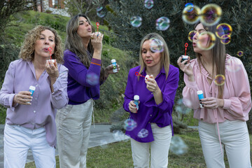 Group of playful women creating soap bubbles in garden.