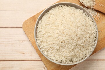 Raw basmati rice in bowl on white wooden table, top view. Space for text