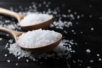 Fototapeta na wymiar Organic salt in spoons on black wooden table, closeup. Space for text