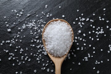 Organic white salt and spoon on black table, top view