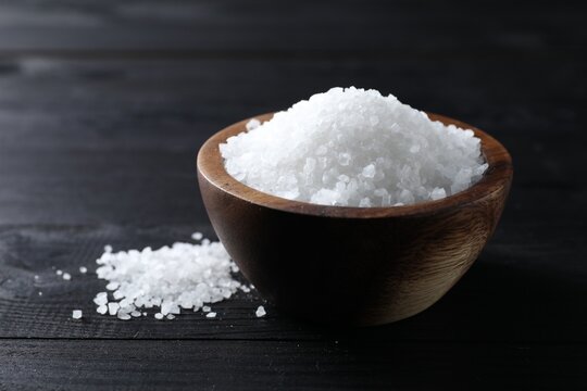 Organic salt in bowl on black wooden table, closeup