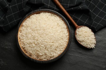 Raw basmati rice in bowl and spoon on black table, top view